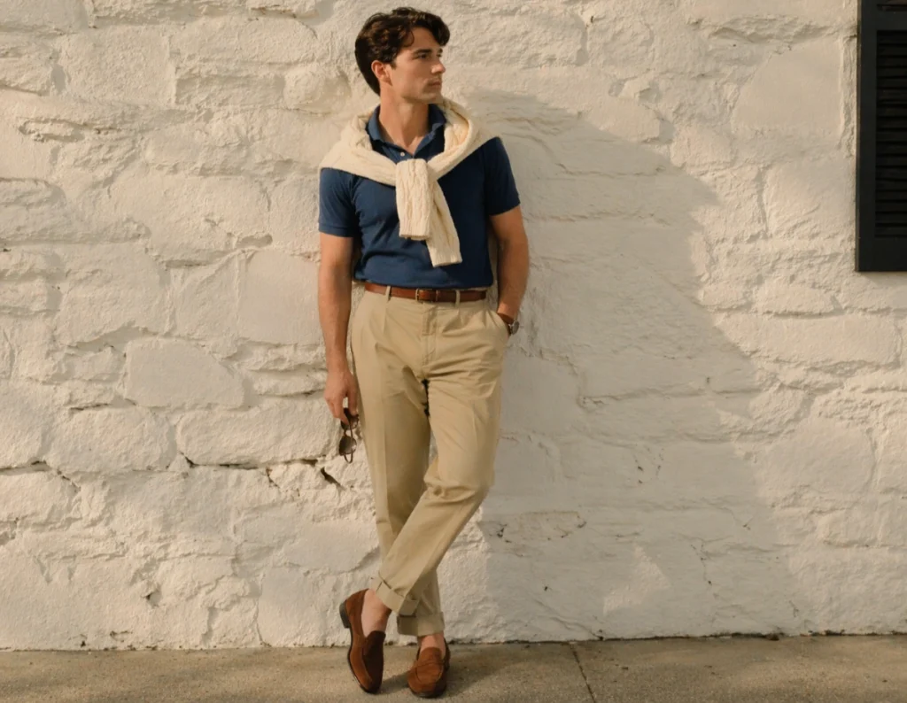 man in modern preppy outfit with navy polo and khakis standing by white wall